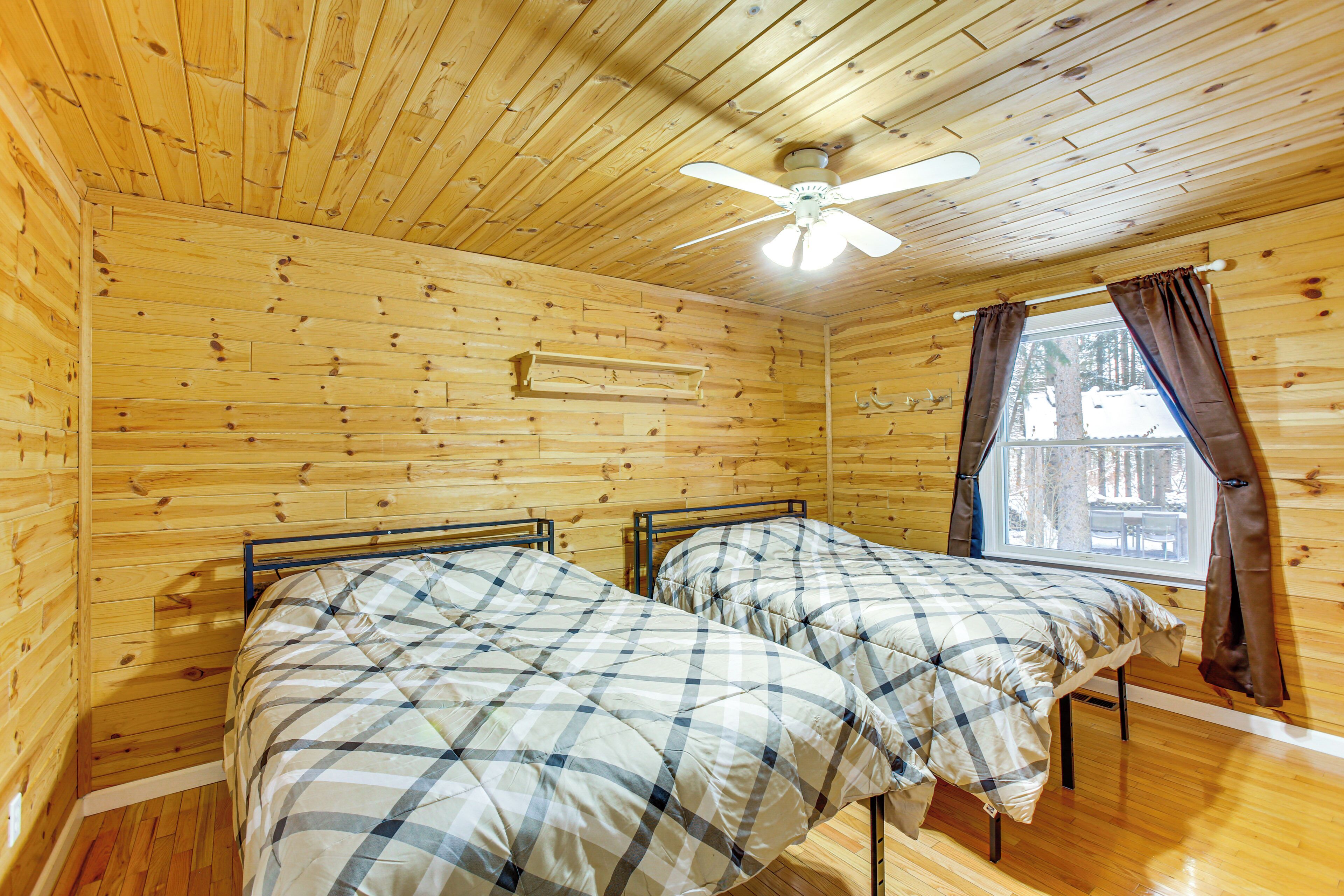 Eine Hütte mit zwei Betten, Holzwänden, einem Deckenventilator und einem Fenster mit Vorhängen.