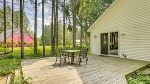 A wooden deck with a table and chairs, surrounded by trees and a house. - Golf Getaway in Cadillac: Deck + Putting Green (Cadillac)
