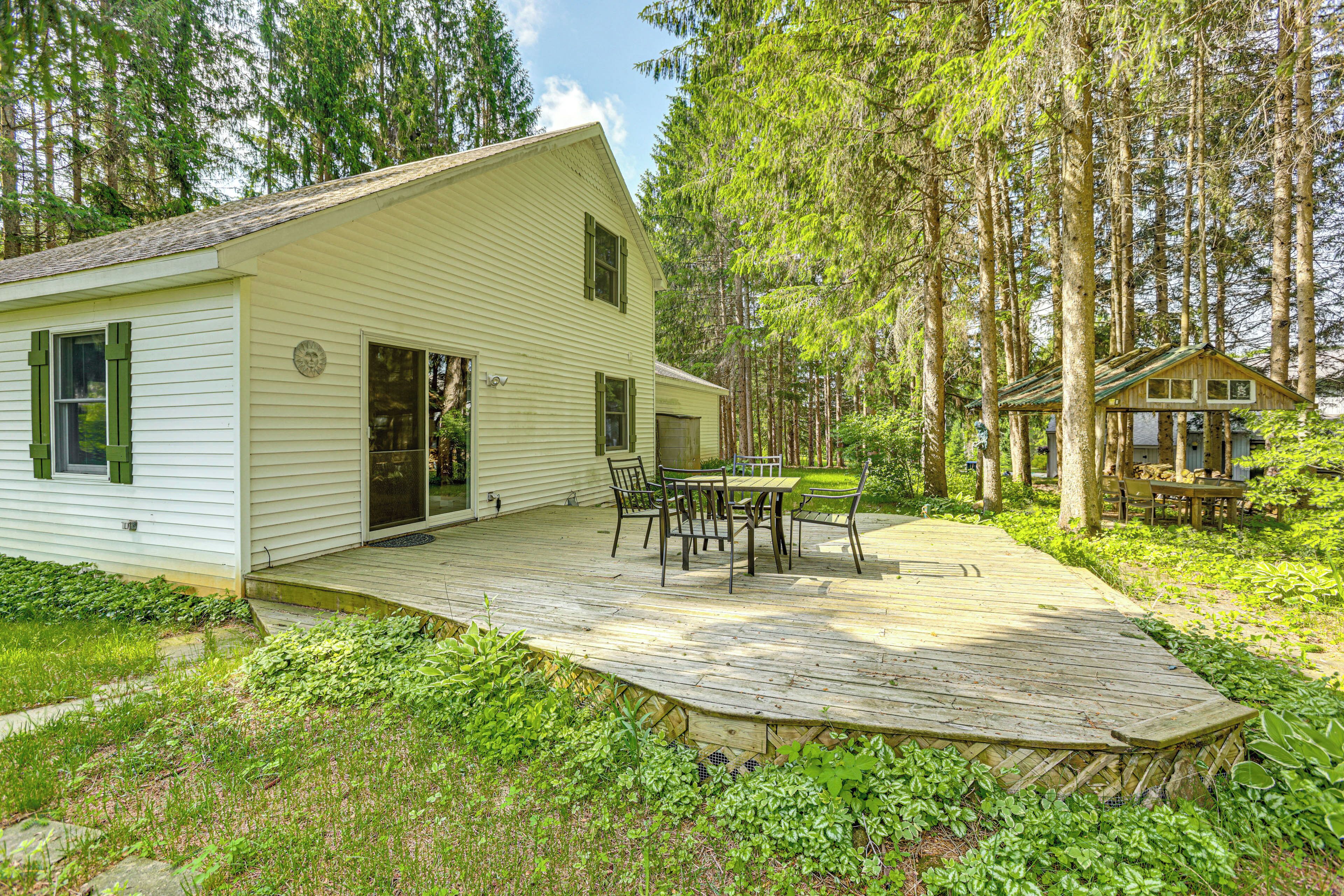 A white cabin with a deck, surrounded by dense forest.