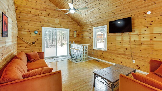 A cozy cabin interior with a wooden ceiling, a ceiling fan, a flat-screen TV, a sofa, a coffee table, and a bar area. - Golf Getaway in Cadillac: Deck + Putting Green (Cadillac)