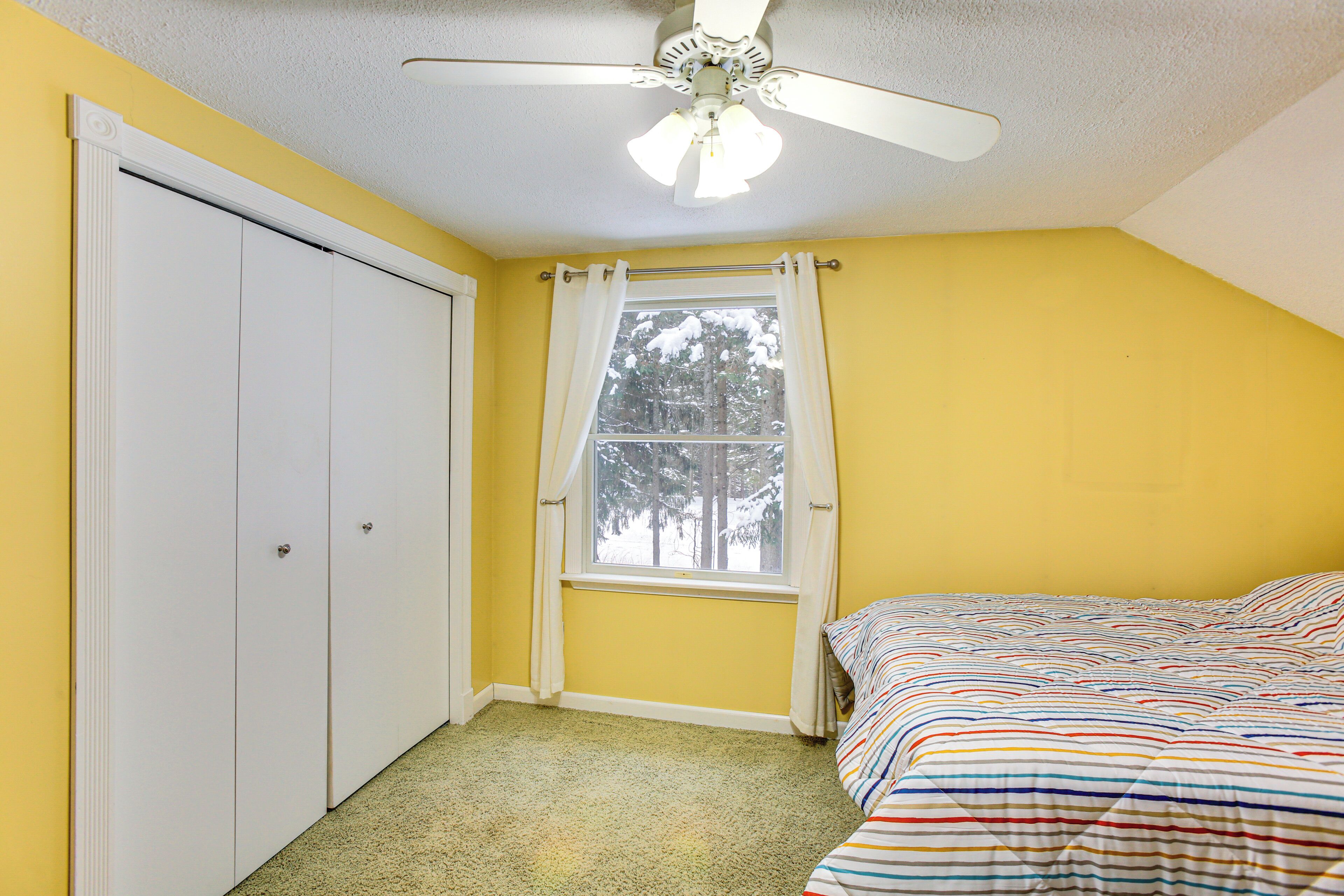A bedroom with a bed, a window with curtains, a ceiling fan, and a wardrobe.