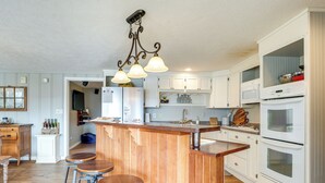 Eine Küche mit Holzhockern, weißen Schränken, einem eingebauten Backofen und einer Pendelleuchte.