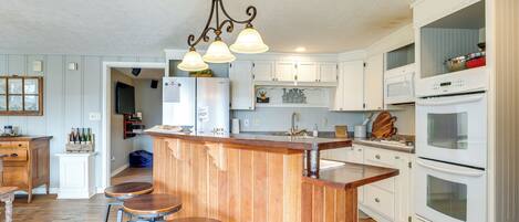 A kitchen with wooden bar stools, white cabinets, a built-in oven, and a hanging light fixture.