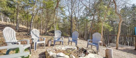 A campsite with several Adirondack chairs arranged around a fire pit, surrounded by trees.