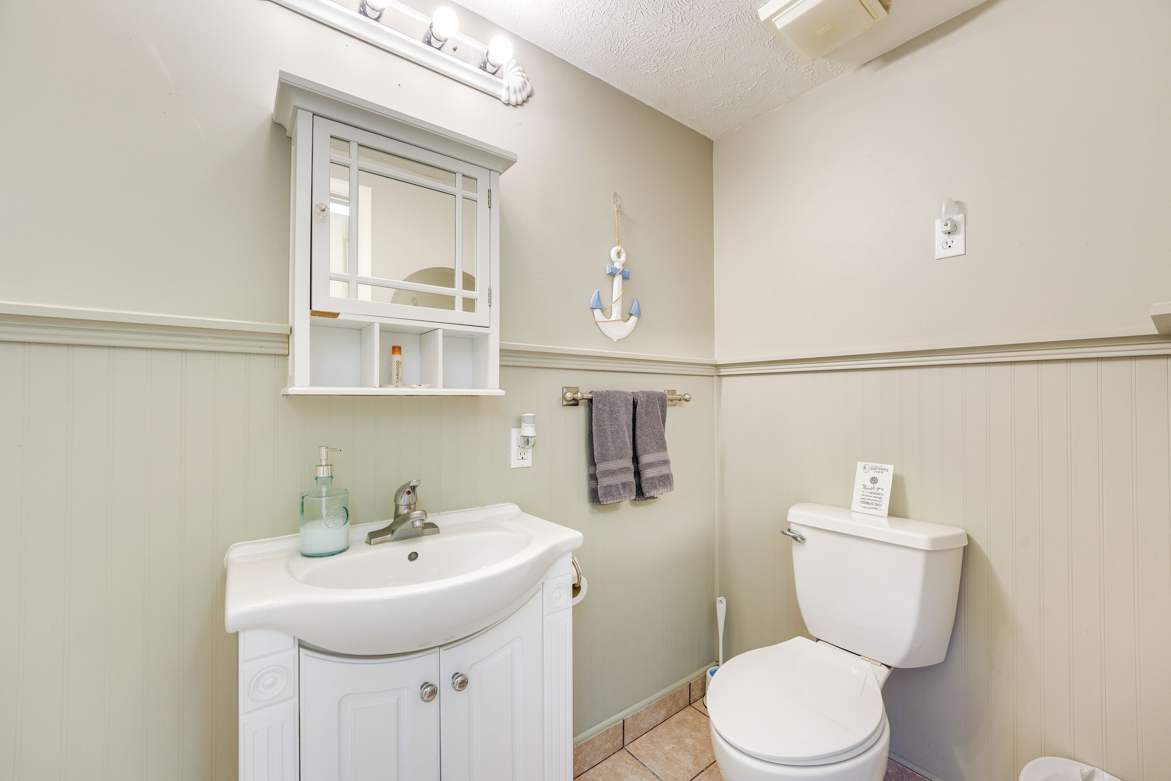 Une salle de bain avec un lavabo blanc, des toilettes et un miroir au-dessus du lavabo.