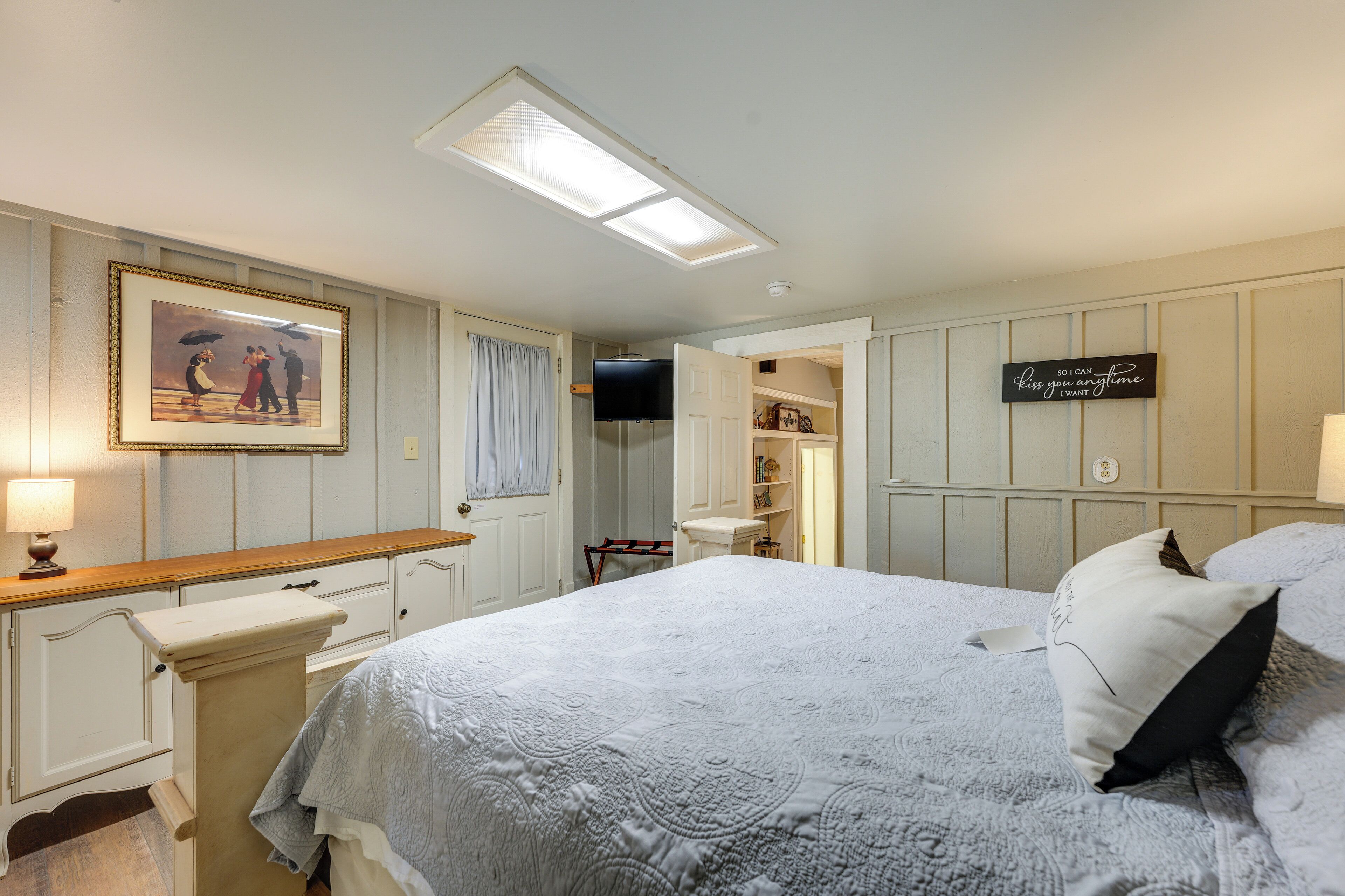 Een slaapkamer met een bed, een dressoir, een kaptafel, een spiegel, een televisie en een bord op de muur.