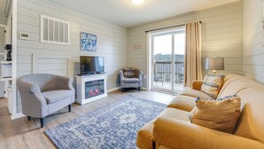 A living room with a grey armchair, a beige sofa, a blue patterned rug, a television, and a window with curtains. - Fish, Boat & Hike On-site: Cape Fair Apartment! (Cape Fair)