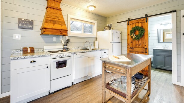 A kitchen with white cabinetry, a wooden stove, a dishwasher, a refrigerator, and a wooden table with a cutting board. - Fish, Boat & Hike On-site: Cape Fair Apartment! (Cape Fair)