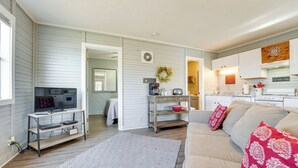 A living room with a TV, sofa, and a kitchen area in the background. - Lake Views & On-site Hiking: Cape Fair Cottage (Cape Fair)