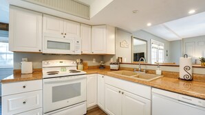 Una cucina con mobili bianchi, forno a microonde integrato, fornello e lavello.