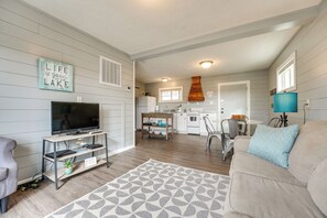 A living room with a TV, sofa, and coffee table. There is a kitchen in the background with a stove, sink, and cabinets. - Lake & Trail Access: Cape Fair Cottage w/ Deck (Cape Fair)