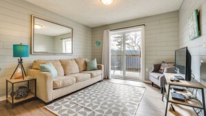 A living room with a beige sofa, a coffee table, a TV, and a sliding glass door leading to a balcony. - Lake & Trail Access: Cape Fair Cottage w/ Deck (Cape Fair)