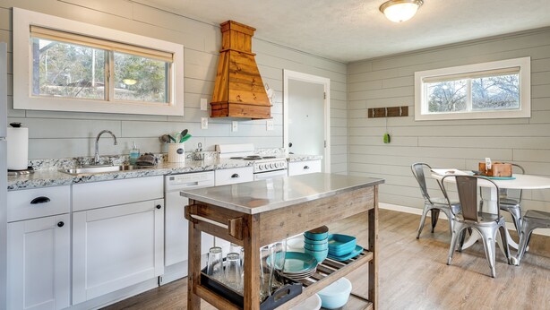 A kitchen with white cabinets, a wooden table, and a window overlooking a snowy landscape. - Lake & Trail Access: Cape Fair Cottage w/ Deck (Cape Fair)