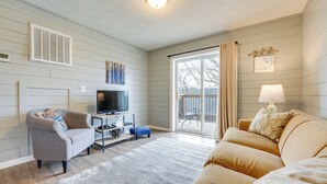 A living room with a grey armchair, a beige sofa, a TV on a stand, and a sliding glass door leading to a balcony. - Walk to Lake & Trails: Cape Fair Retreat w/ Grill! (Cape Fair)