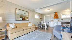 A living room with a beige sofa, a gray rug, a dining table with chairs, a kitchen area with a stove, and a large mirror on the wall. - Walk to Lake & Trails: Cape Fair Retreat w/ Grill! (Cape Fair)
