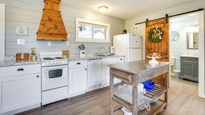 A kitchen with white cabinets, a wooden stove, a dishwasher, a sink, and a wooden table with blue bowls. - Walk to Lake & Trails: Cape Fair Retreat w/ Grill! (Cape Fair)