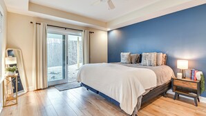 A bedroom with a bed, a nightstand, a lamp, a mirror, and a view through a glass door.