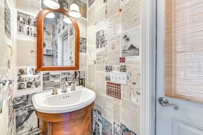 A bathroom with a copper sink, a mirror with three lights, and walls covered with various photographs and newspaper clippings. - Mountain Views & Fire Pit: Sandgate Getaway (Arlington)