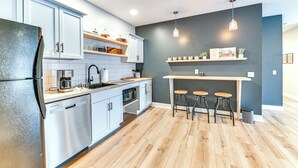 A modern kitchen with white cabinets, a stainless steel refrigerator, wooden stools, and a dark accent wall.
