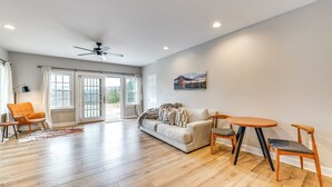 A spacious living room with hardwood flooring, a sofa, two chairs, a coffee table, and a ceiling fan.