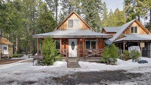 A wooden cabin with a porch, surrounded by trees and snow.