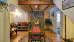 Un accogliente soggiorno con parete in pietra, travi in legno a soffitto, un tavolo da pranzo con sedie, un divano e una televisione.