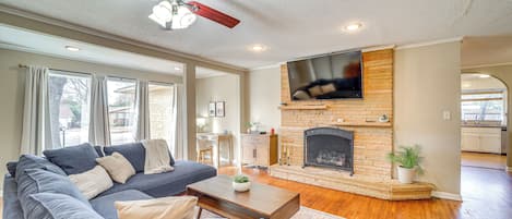 A living room with a sofa, coffee table, fireplace, TV, and a ceiling fan.