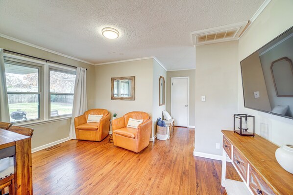 A spacious living room with hardwood flooring, a large window, a sofa, a TV, and a wooden cabinet.