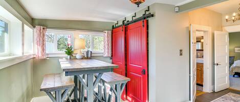 Una cocina con una mesa de madera y bancos, una puerta roja y un candelabro.
