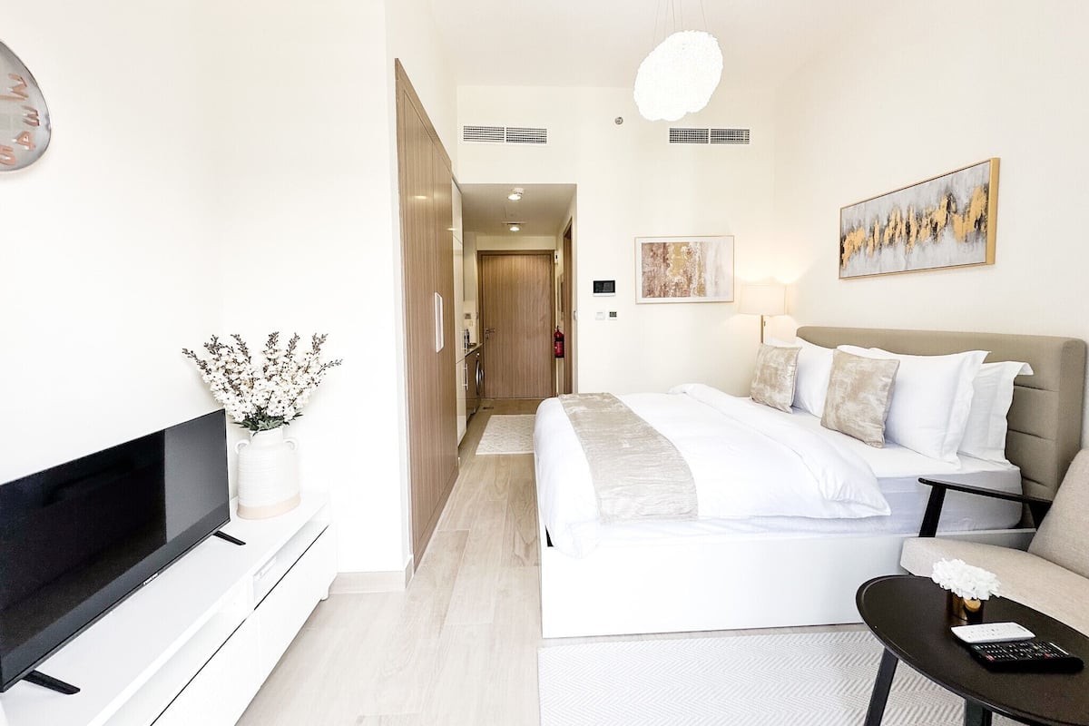 A modern hotel room with a flat-screen TV, a bed with white bedding, a sofa, a coffee table, and a painting on the wall.