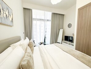 A hotel room with a large bed, a TV, a mirror, and a window with curtains.