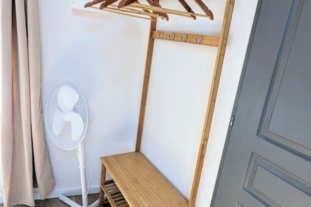 A corner room with a wooden bench, a white fan, and a clothes drying rack.
