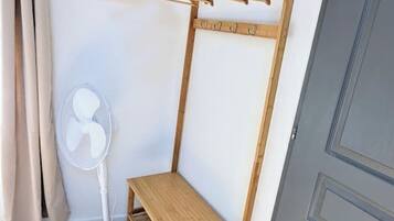 A corner room with a wooden bench, a white fan, and a clothes drying rack.