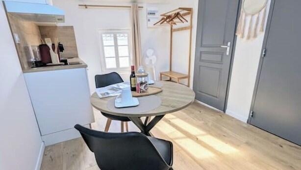 A compact room with a round dining table, a black chair, a small kitchenette, and a door with a coat rack. - Studio 5: Your urban oasis.  (Gond-Pontouvre)