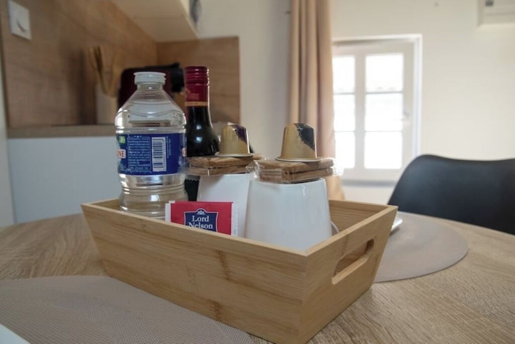 Un plateau en bois avec une bouteille d’eau, une bouteille de vin, un morceau de fromage et un paquet de collations, le tout posé sur une table.