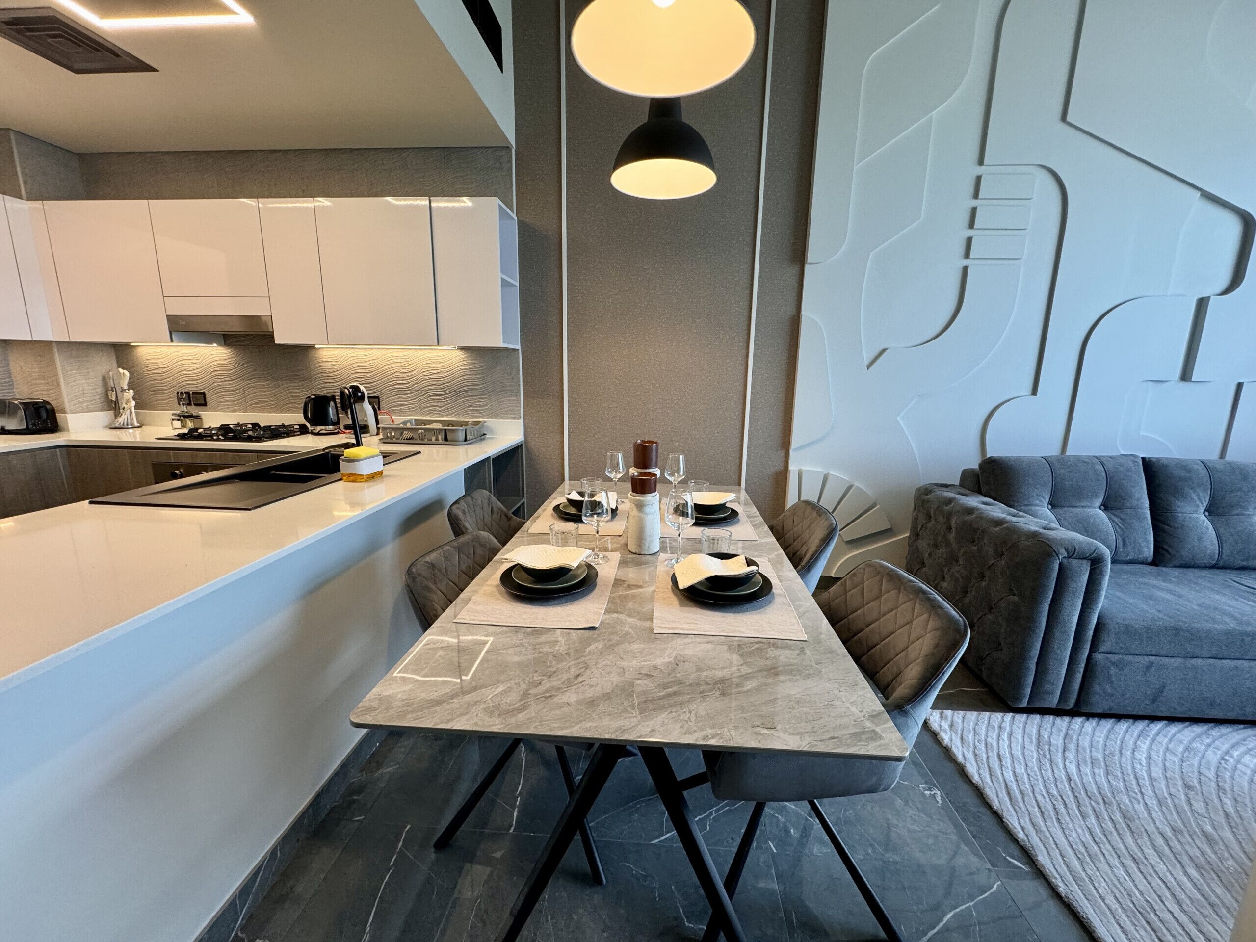 Een moderne keuken met een eethoek, met een marmeren aanrechtblad, zwarte stoelen en een grijze bank.