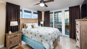 Une chambre à coucher avec un grand lit, une table de chevet en bois, une commode et un ventilateur de plafond.