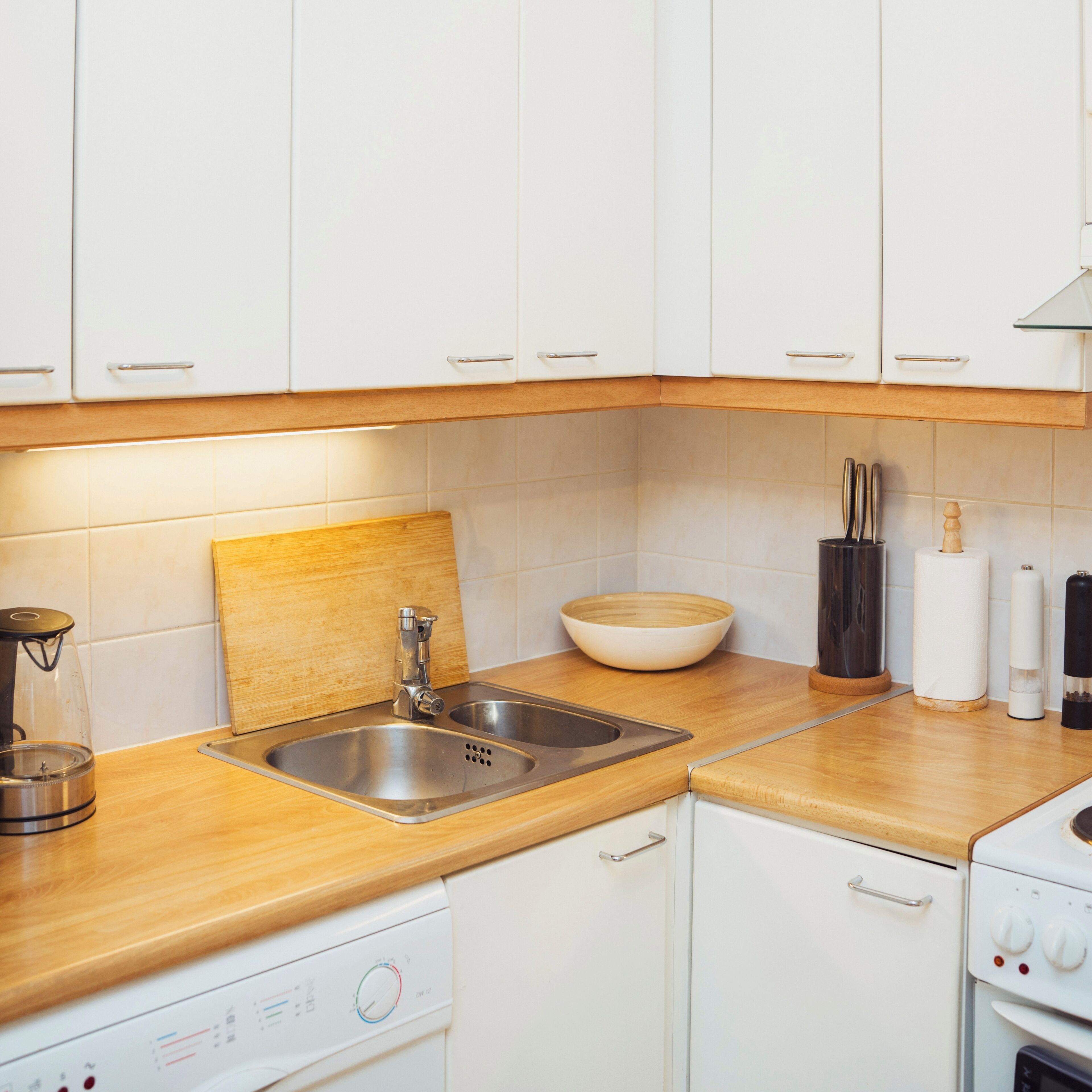 Eine Küche mit weißen Schränken, einer Holz Arbeitsplatte, einer Edelstahlspüle, einem Geschirrspüler und einem Backofen.