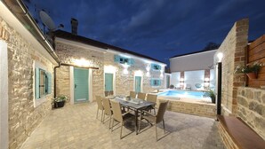 A courtyard with a pool, stone walls, a dining table with chairs, and a wooden bench. - Villa Lapis (Sveti Filip i Jakov)