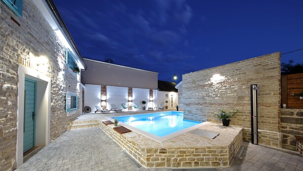 A stone pool with a surrounding patio, a wooden door, and a stone wall. - Villa Lapis (Sveti Filip i Jakov)