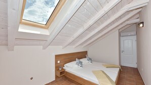 A bedroom with a skylight, wooden beams, a bed with pillows, a bedside table, and a door. - Villa Lapis (Sveti Filip i Jakov)