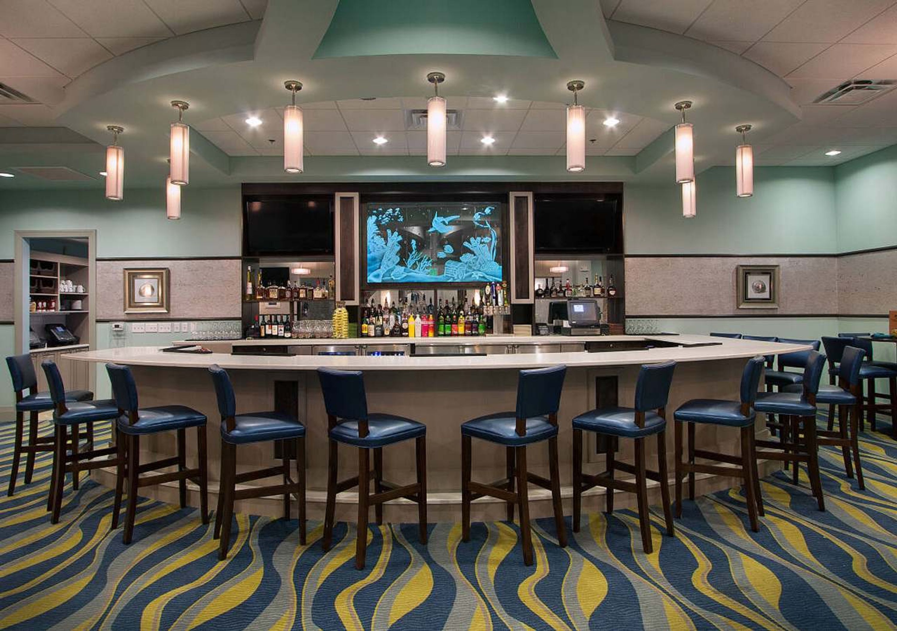 A bar area with a circular bar, multiple bar stools, and a large screen displaying an underwater scene.