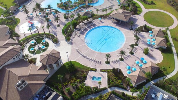 An aerial view of a resort with a central swimming pool, multiple smaller pools, and a variety of outdoor seating areas surrounded by palm trees and greenery. - Upstay Luxury Living w Pool Hot Tub Cinema (Davenport)