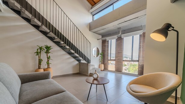 A modern living room with a grey sofa, a round table, a floor lamp, and a staircase. - W Contemporary Loft w AC in Trendy Laureles (Medellín)