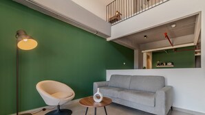 A modern living room with a green wall, a grey sofa, a round wooden coffee table, a white vase, and a floor lamp. - W Contemporary Loft w AC in Trendy Laureles (Medellín)