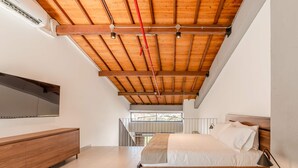 A modern bedroom with a wooden ceiling, a bed, a bedside table, a nightstand, a TV mounted on the wall, and a view of the outdoors. - W Contemporary Loft w AC in Trendy Laureles (Medellín)