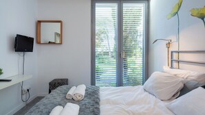 Un dormitorio con cama, televisor montado en la pared, ventana con persianas y espejo.