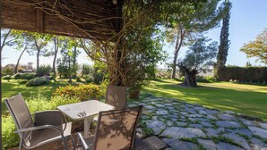 Un patio al aire libre con una mesa y sillas, rodeado de un sendero de piedra y exuberante vegetación.