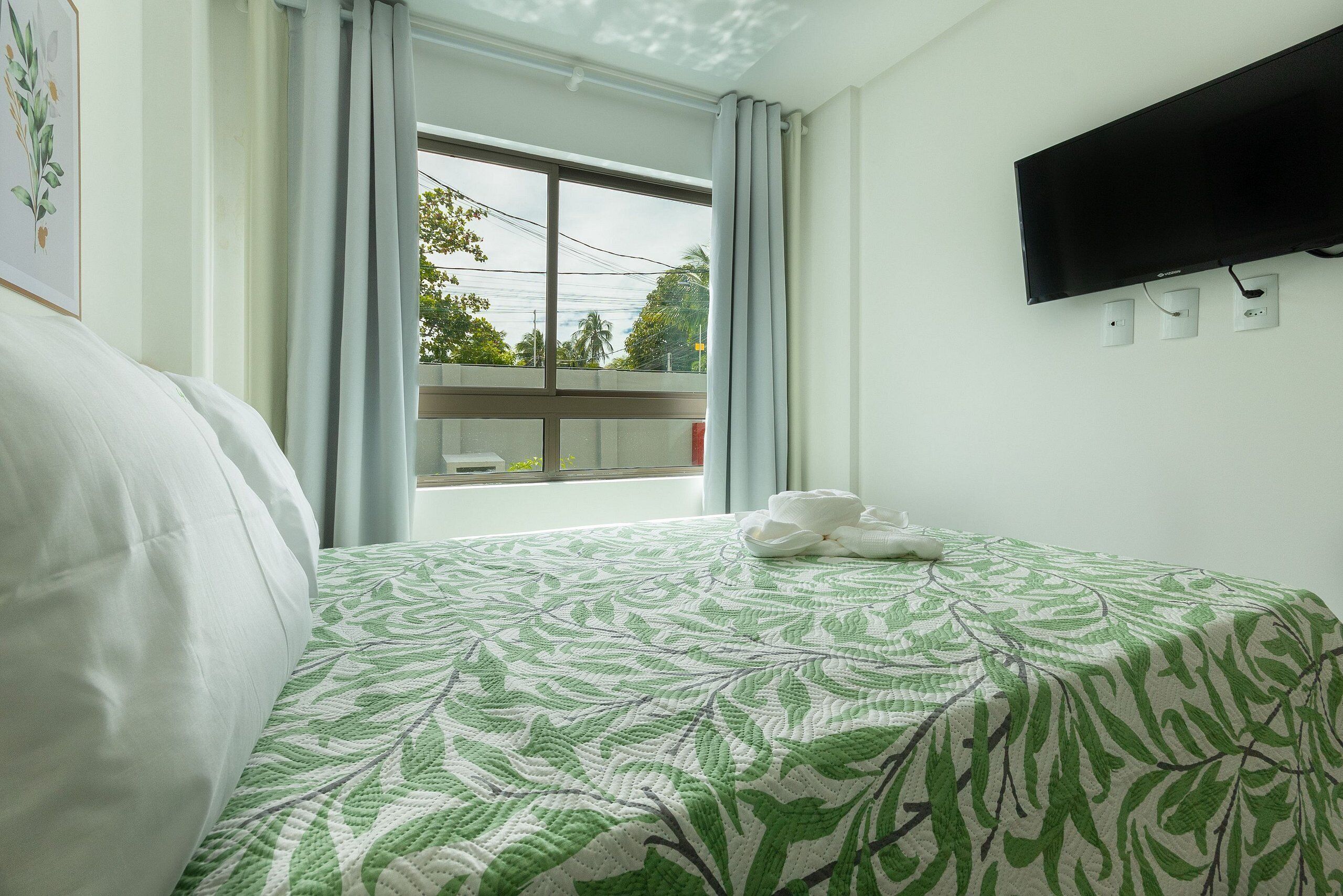 Habitación de hotel con cama, televisor de pantalla plana montado en la pared y ventana con cortinas.
