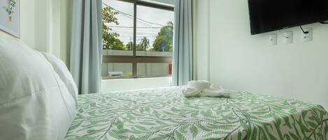 Habitación de hotel con cama, televisor de pantalla plana montado en la pared y ventana con cortinas.